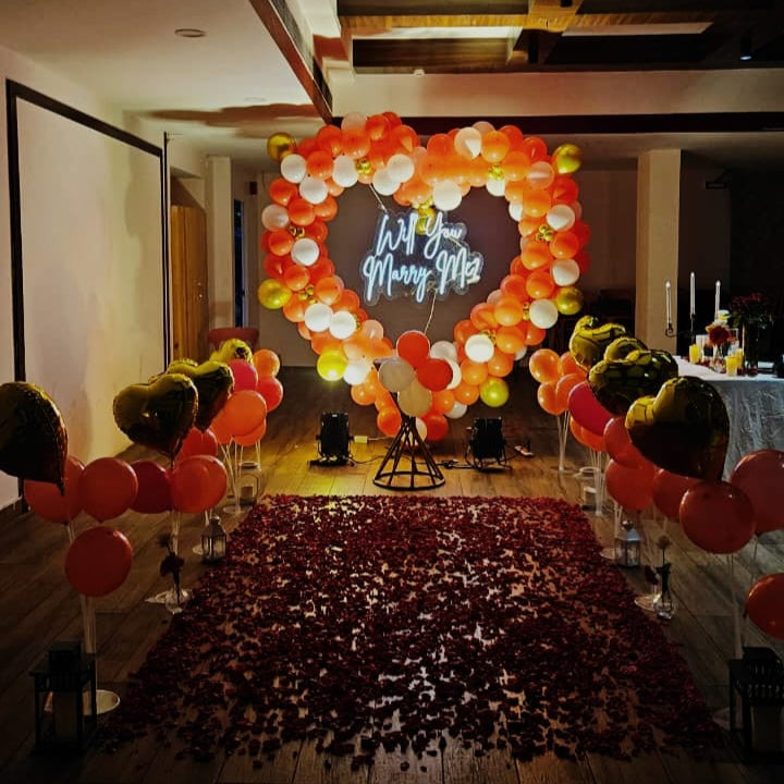 Romantic marriage proposal decoration in Hyderabad with a heart‑shaped balloon arch, glowing “Will You Marry Me” LED neon sign, and rose petal carpet.