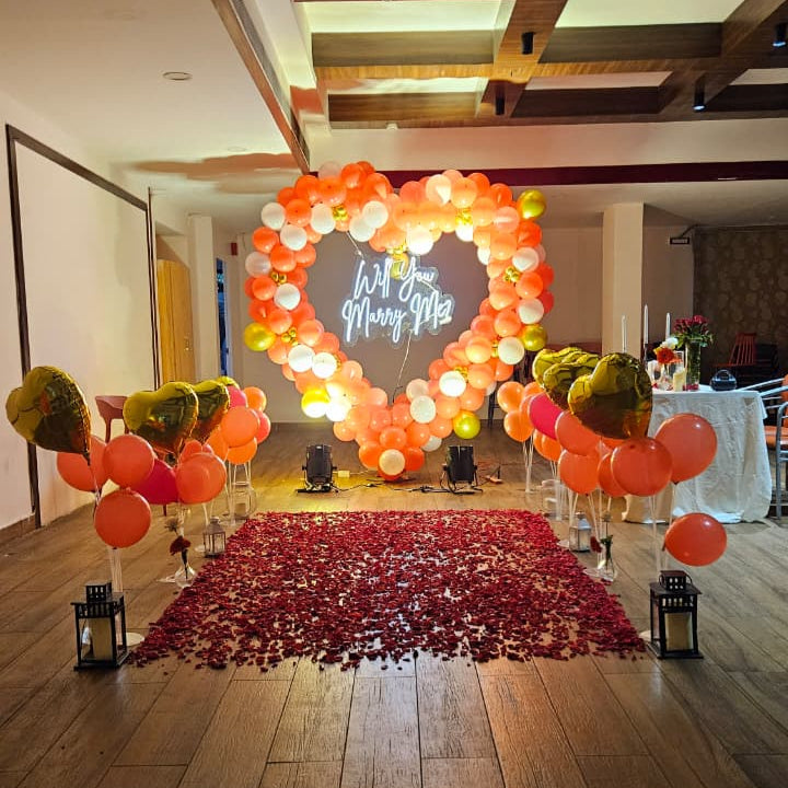 Romantic marriage proposal decoration in Hyderabad with a heart‑shaped balloon arch, glowing “Will You Marry Me” LED neon sign, and rose petal carpet.