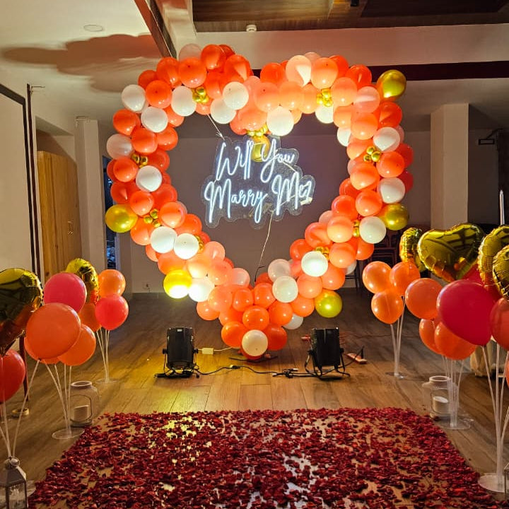 Romantic marriage proposal decoration in Hyderabad with a heart‑shaped balloon arch, glowing “Will You Marry Me” LED neon sign, and rose petal carpet.