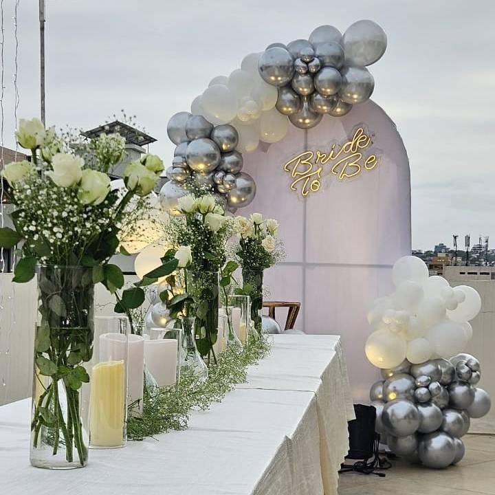 A table adorned with white roses and candles, surrounded by twinkling fairy lights, creating a romantic ambiance for an event.