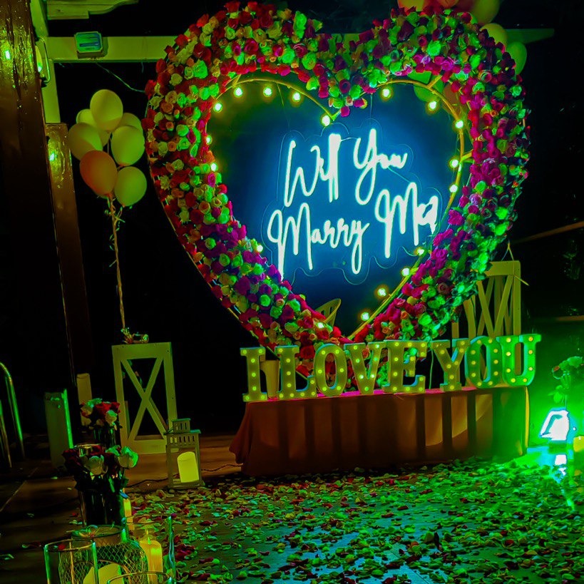 Romantic poolside candle light dinner in Hyderabad with a rose bouquet, neon lights, and optional photography add-ons.