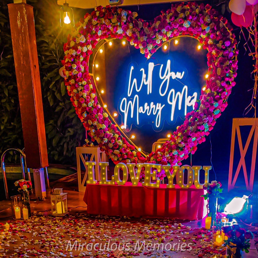 Romantic 'Will You Marry Me' neon light setup for a candle light dinner in Hyderabad at a private poolside venue.