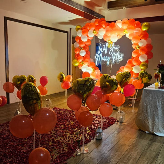 Romantic marriage proposal decoration in Hyderabad with a heart‑shaped balloon arch, glowing “Will You Marry Me” LED neon sign, and rose petal carpet.