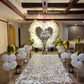 A romantic proposal setup featuring a heart-shaped balloon arch, a "Will You Marry Me?" sign, white flower petals, and golden balloons.