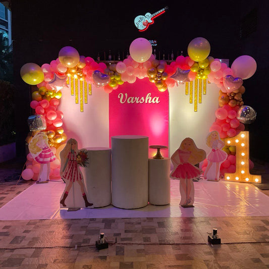 Barbie theme birthday decoration in Hyderabad with pink and gold balloon arch, doll cutouts, and illuminated number 1 stage setup.