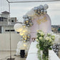 A rooftop bridal shower setup with a "Bride To Be" sign, white and silver balloon arch, and a table decorated with white flowers.